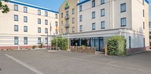 A hotel with a modern facade, multiple windows, and a covered outdoor seating area with benches. - Holiday Inn Express Dortmund by IHG (Dortmund)