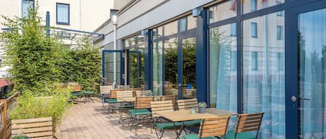 An outdoor seating area with tables and chairs, a glass door entrance, and a building with windows in the background.