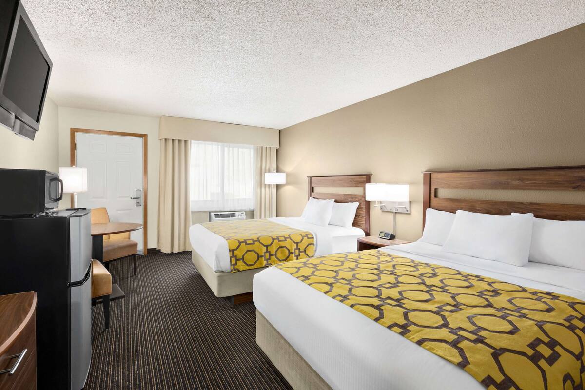 A hotel room with two beds, a desk with a TV, and a window with curtains.