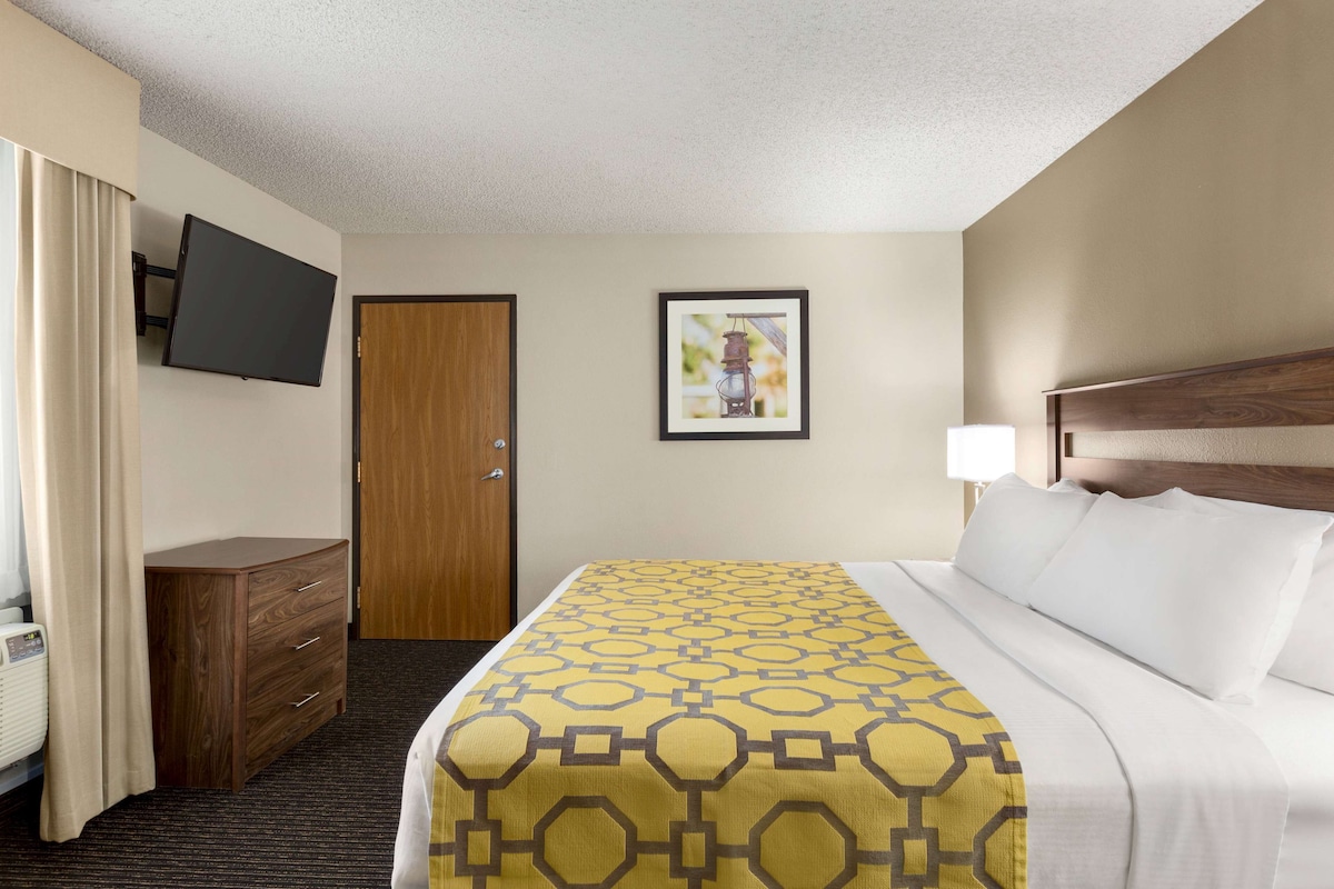 A hotel room with a bed, a TV mounted on the wall, a wooden dresser, a door, and a framed picture on the wall.