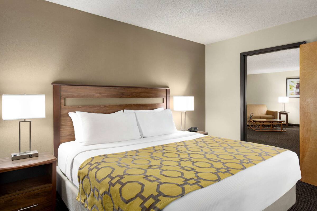 A hotel room with a large bed, two bedside lamps, a wooden headboard, and a patterned throw blanket.