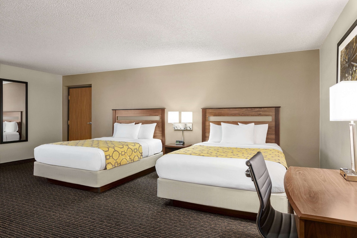 A hotel room with two beds, a desk, a chair, a lamp, and a mirror.