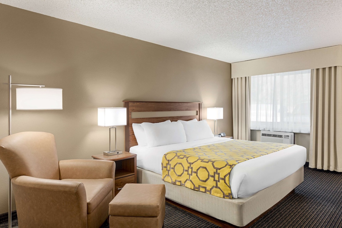 A hotel room with a bed, a chair, a nightstand, and a window with curtains.