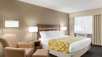 A hotel room with a bed, a chair, a bedside table, and a lamp.