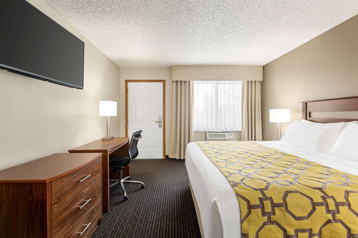 A hotel room with a bed, desk, chair, and a flat-screen TV mounted on the wall.