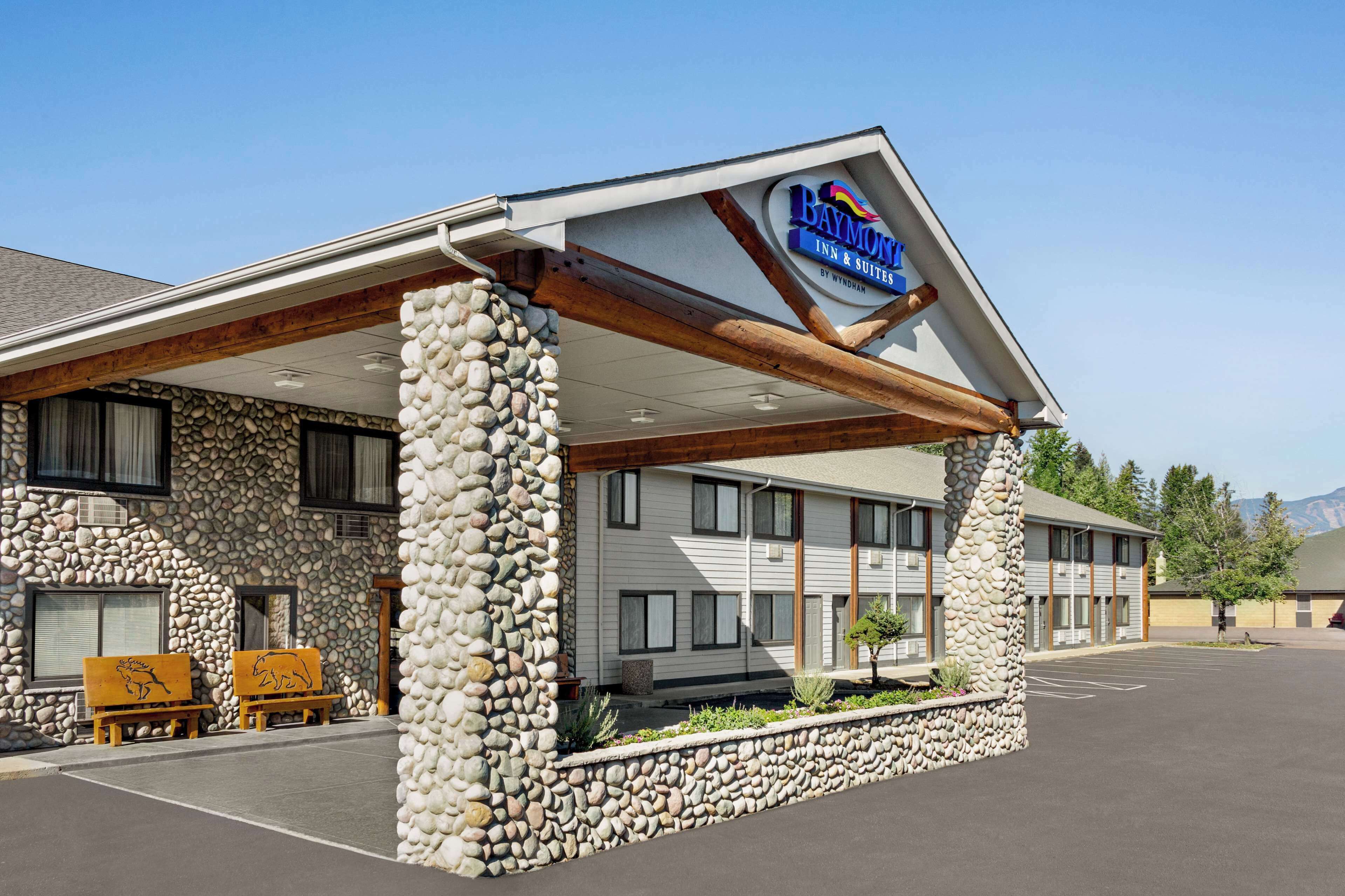 A Baymont Inn & Suites with a stone facade, wooden beams, and a clear sky.