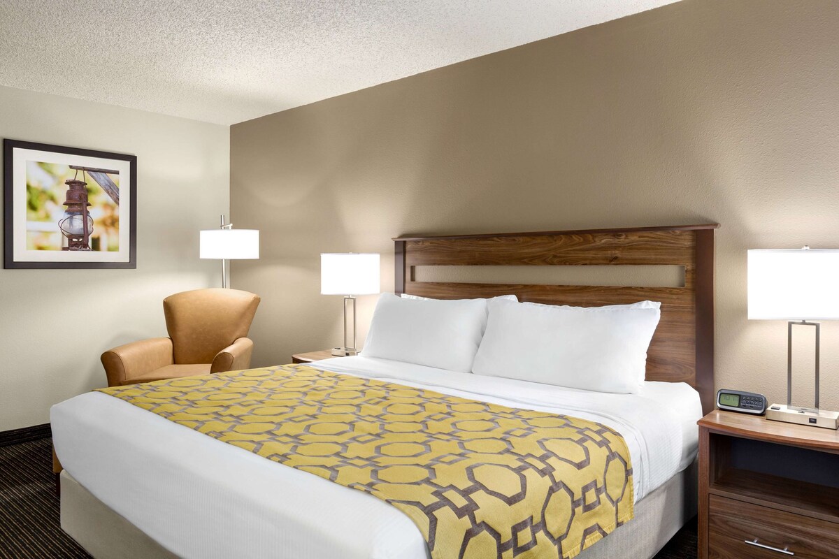 A hotel room with a large bed, a chair, two bedside tables with lamps, and a framed picture on the wall.