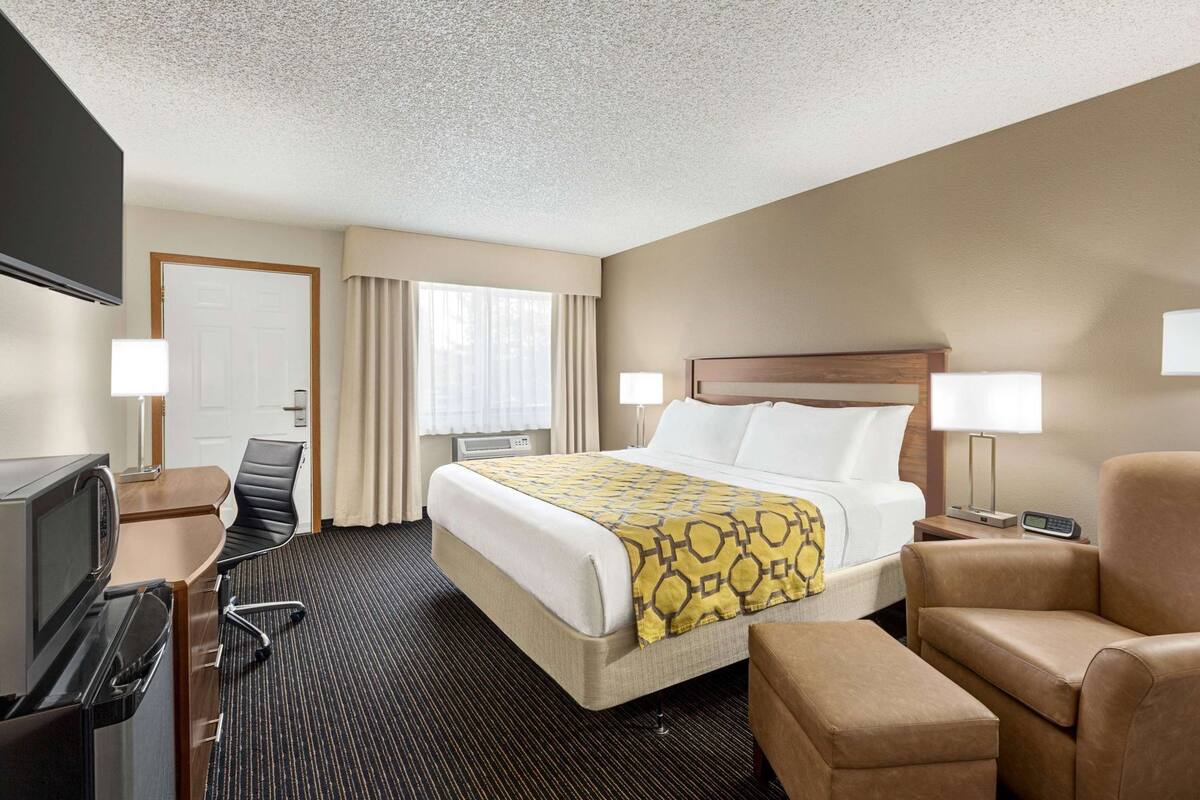 A hotel room with a bed, two bedside lamps, a desk with a TV, a chair, and a small table.