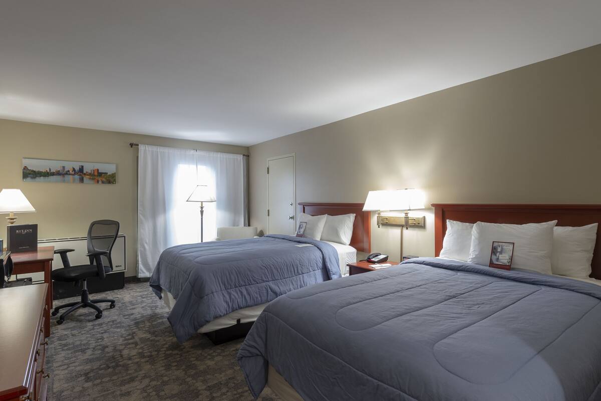 A hotel room with two beds, a desk, a chair, and a nightstand.