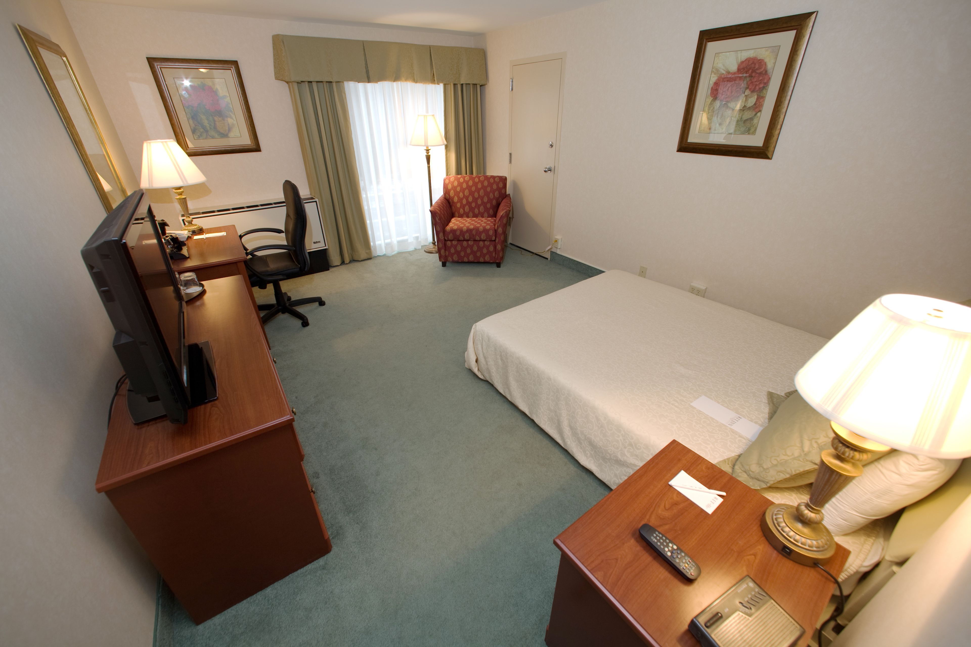 Una habitación de hotel con una cama, un escritorio con computadora, una silla, una lámpara y un televisor.