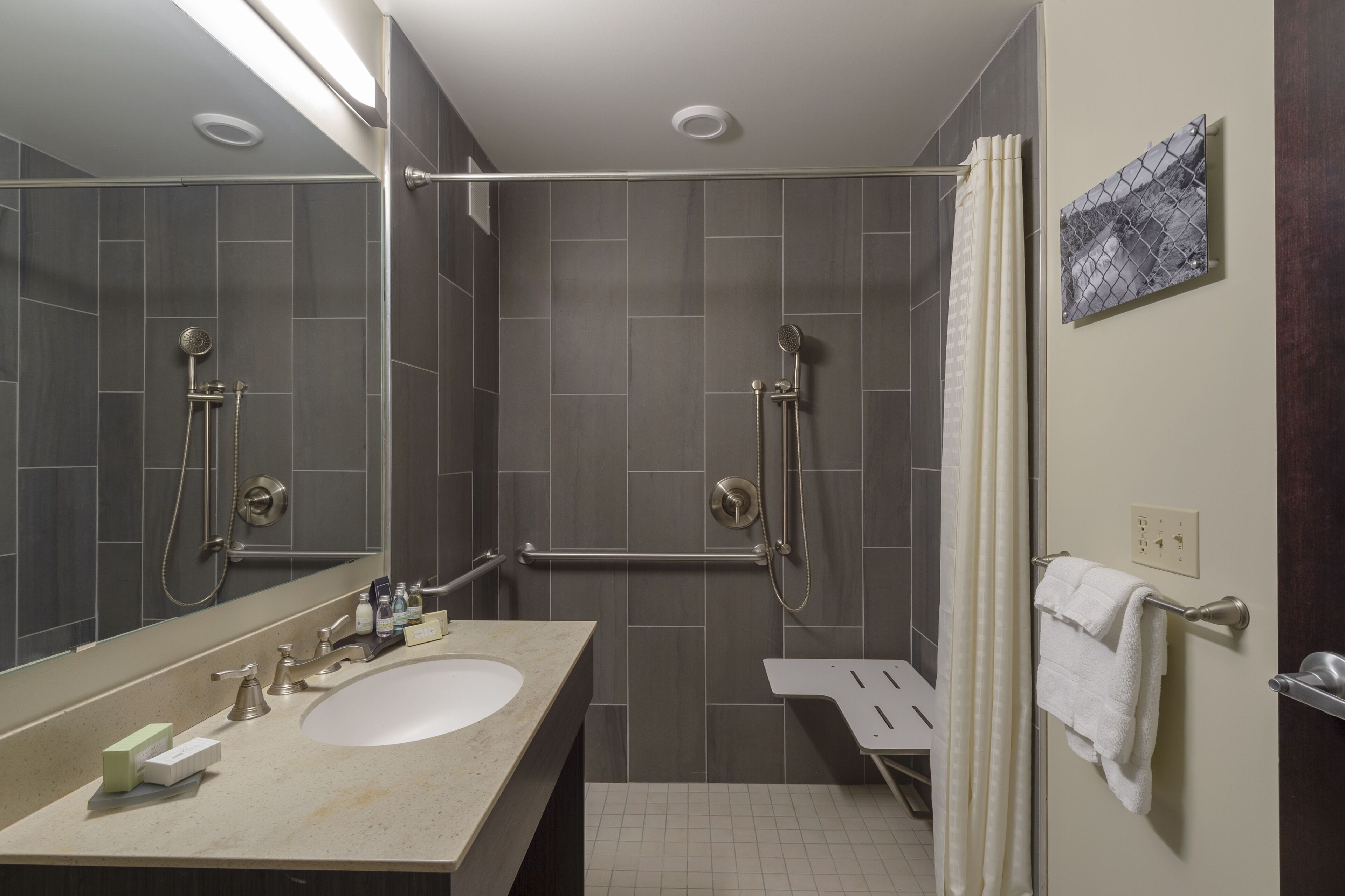A modern bathroom with a large mirror, a sink, a shower with a handheld showerhead, and a towel rack.