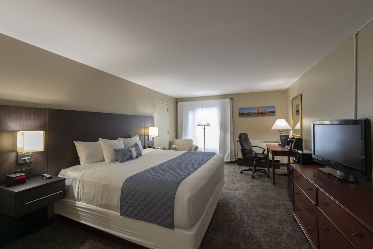 A hotel room with a bed, desk, TV, and a chair.