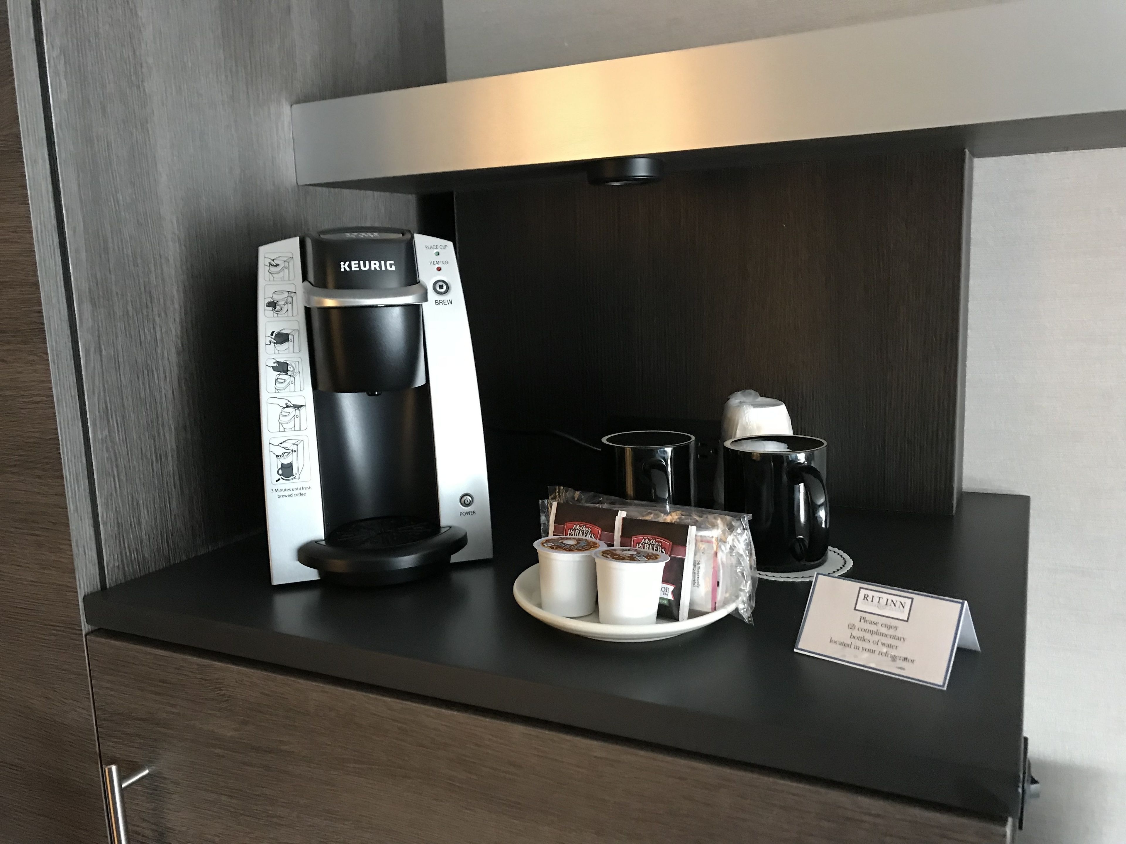 A Keurig coffee maker on a counter with a plate of coffee pods, a mug, and a water jug.