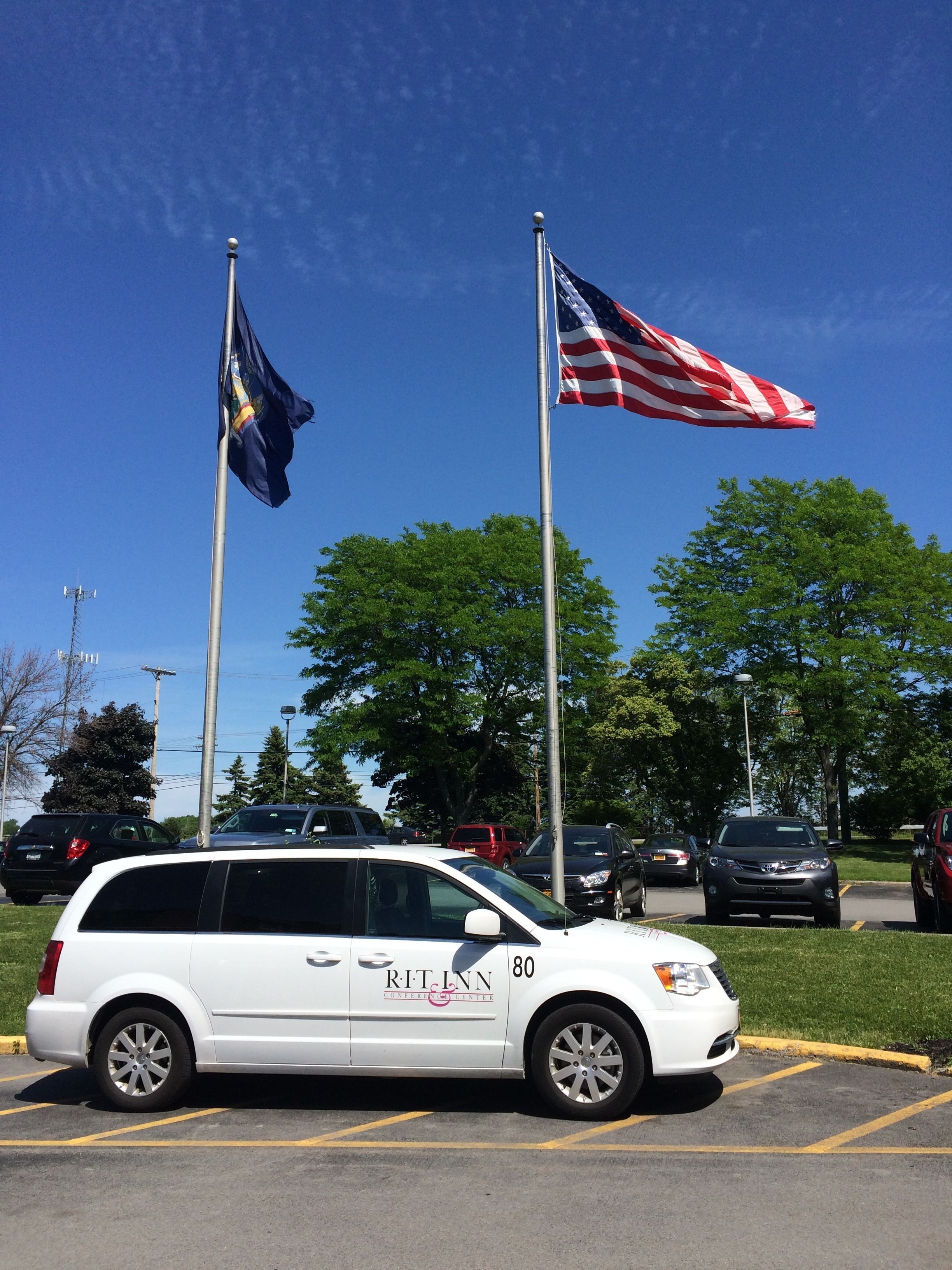 A white minivan parked in a parking lot with a flagpole displaying the American flag and another flag.