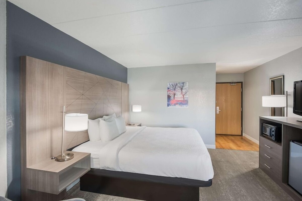 A modern hotel room with a bed, bedside tables, a TV, and a small kitchenette.