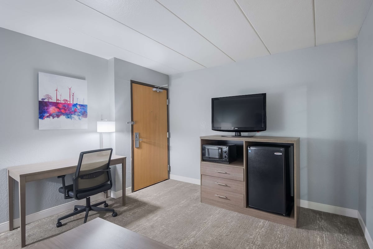 Ein Hotelzimmer mit einem Holztisch, einem schwarzen Bürostuhl, einem Fernseher, einer Mikrowelle und einem Kühlschrank.