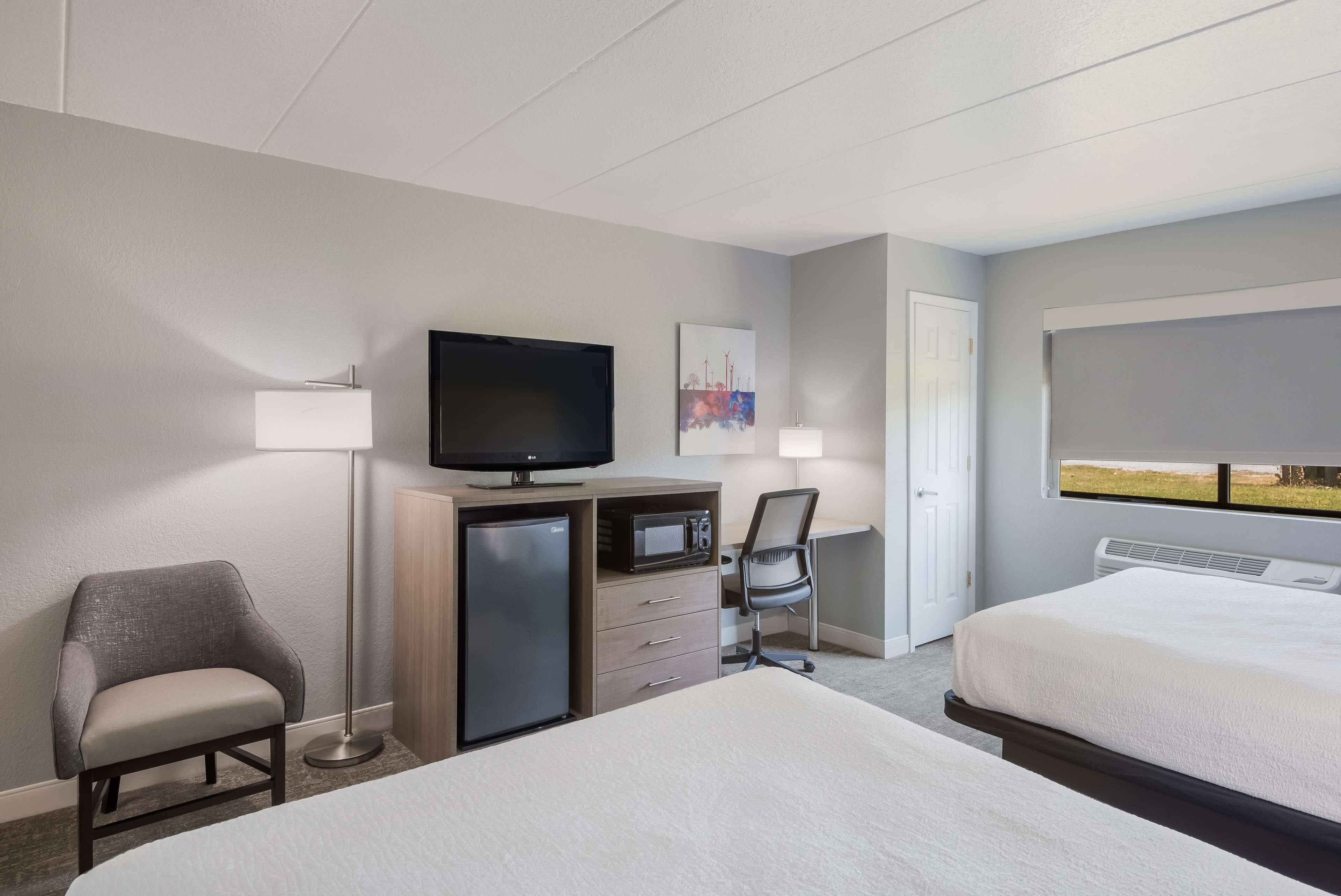 A hotel room with two beds, a desk with a television, a chair, and a small refrigerator.