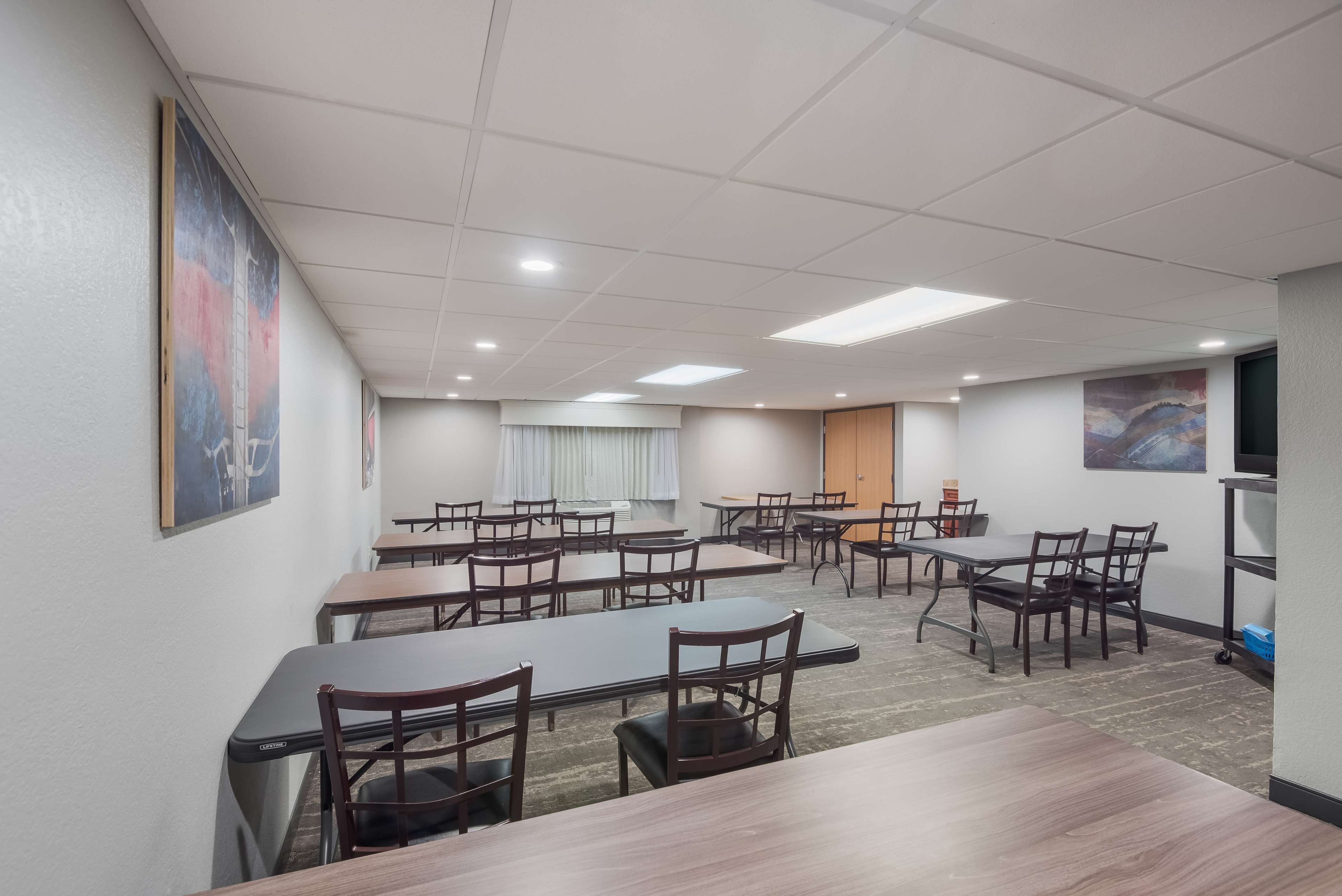 A conference room with multiple tables and chairs, white walls, and ceiling lights.