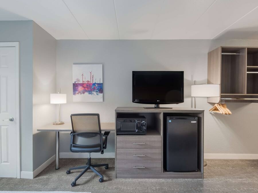 Habitación de hotel con escritorio, silla, televisión, microondas, refrigerador y estante con perchas.