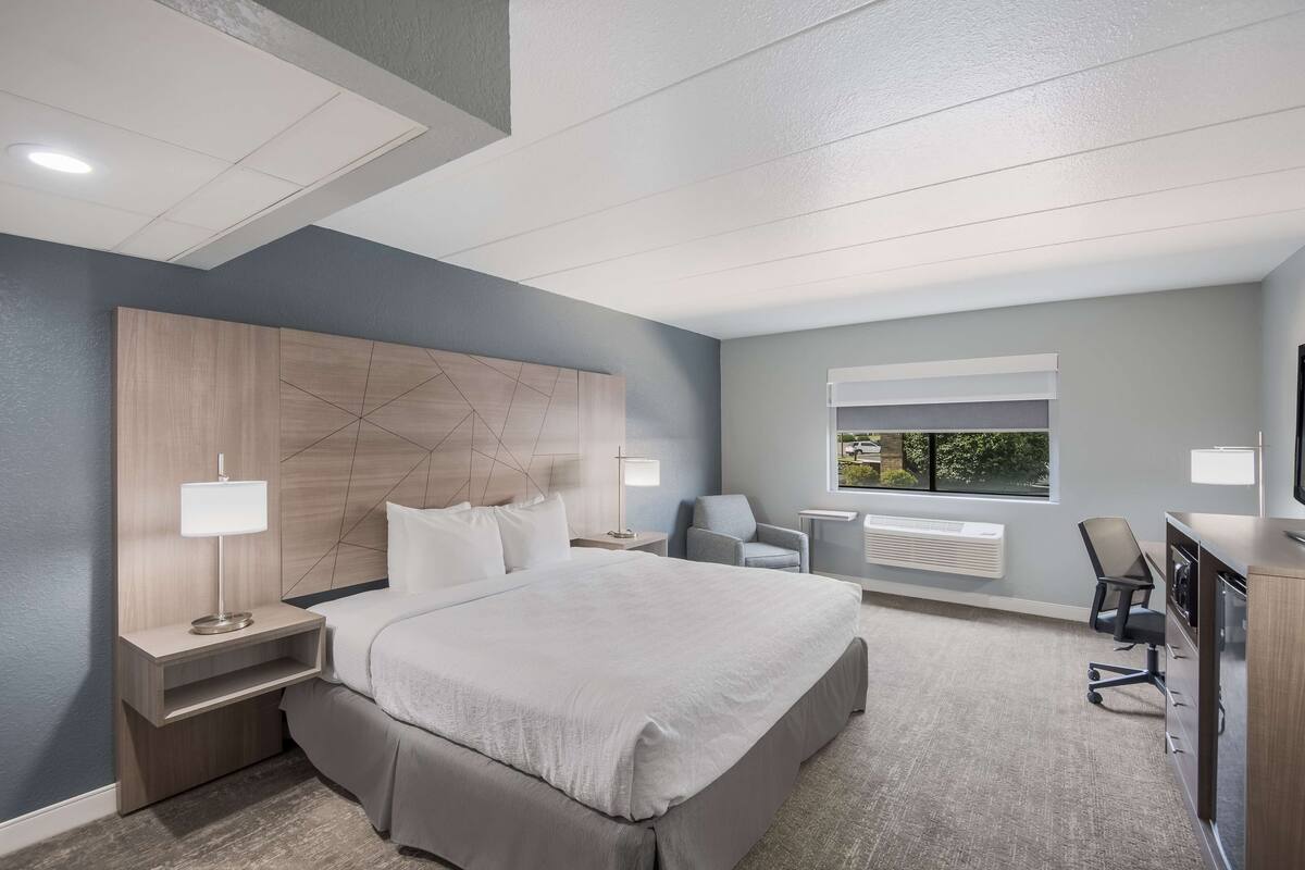 A modern hotel room with a large bed, bedside tables, a desk, and a chair.