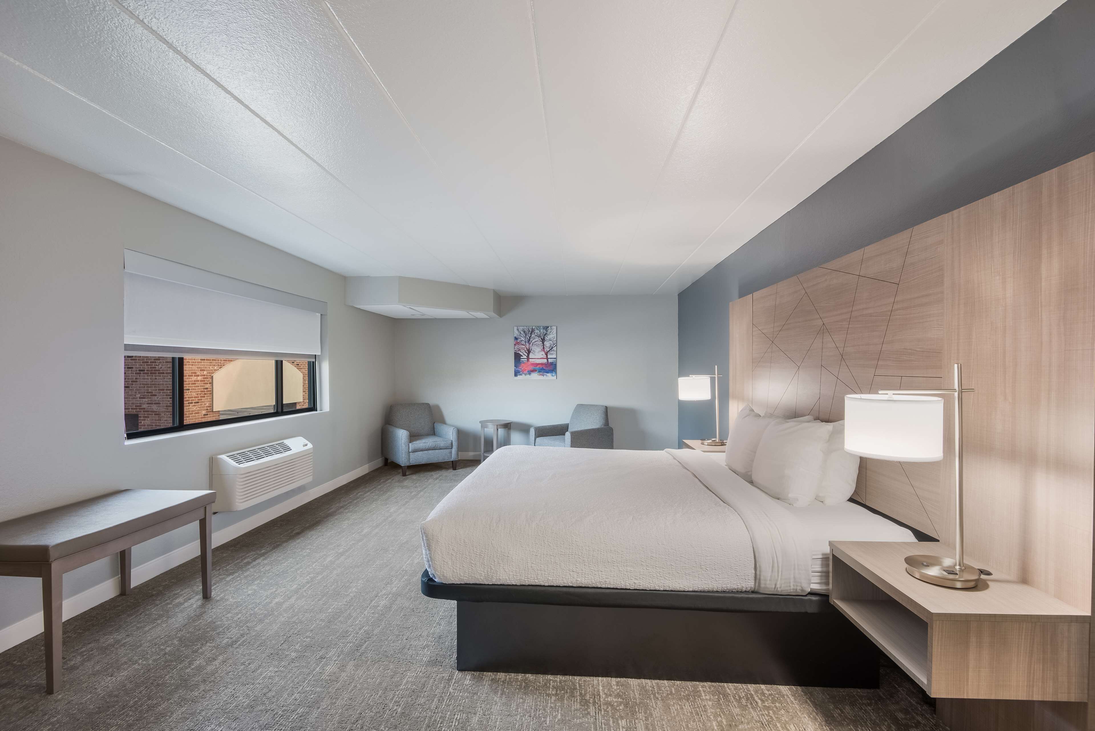 Una camera d'albergo moderna con un letto grande, comodini, una panca e una finestra con tende.