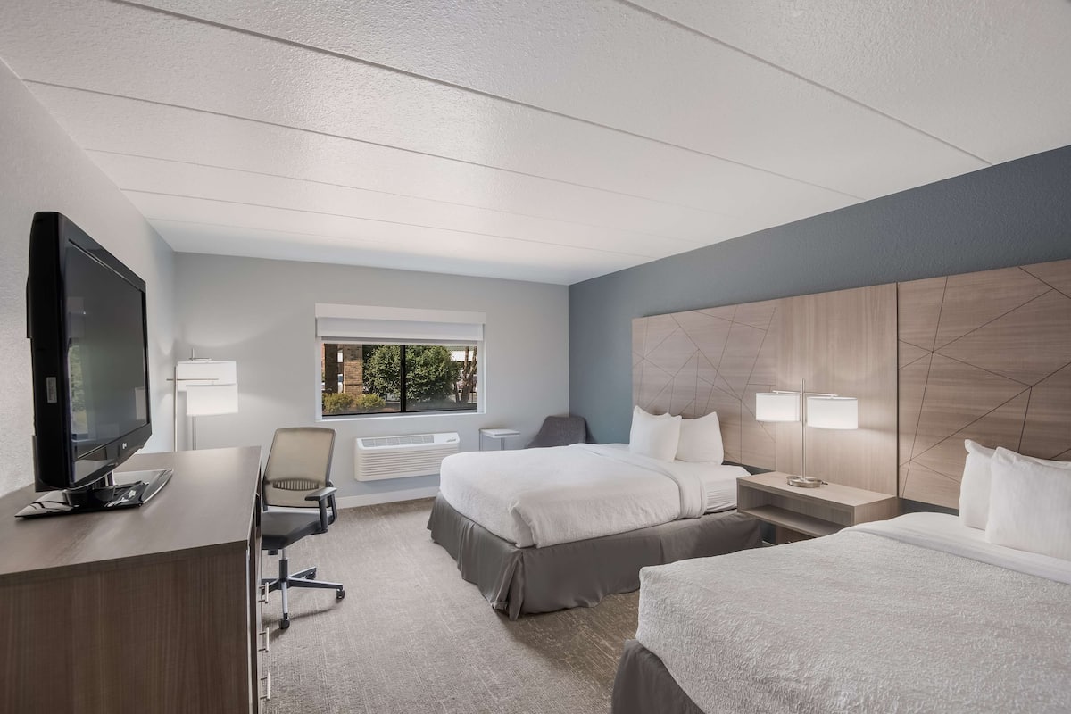Ein Hotelzimmer mit einem großen Bett, einem Schreibtisch mit Fernseher, zwei Nachttischlampen und einem Fenster mit Blick ins Freie.