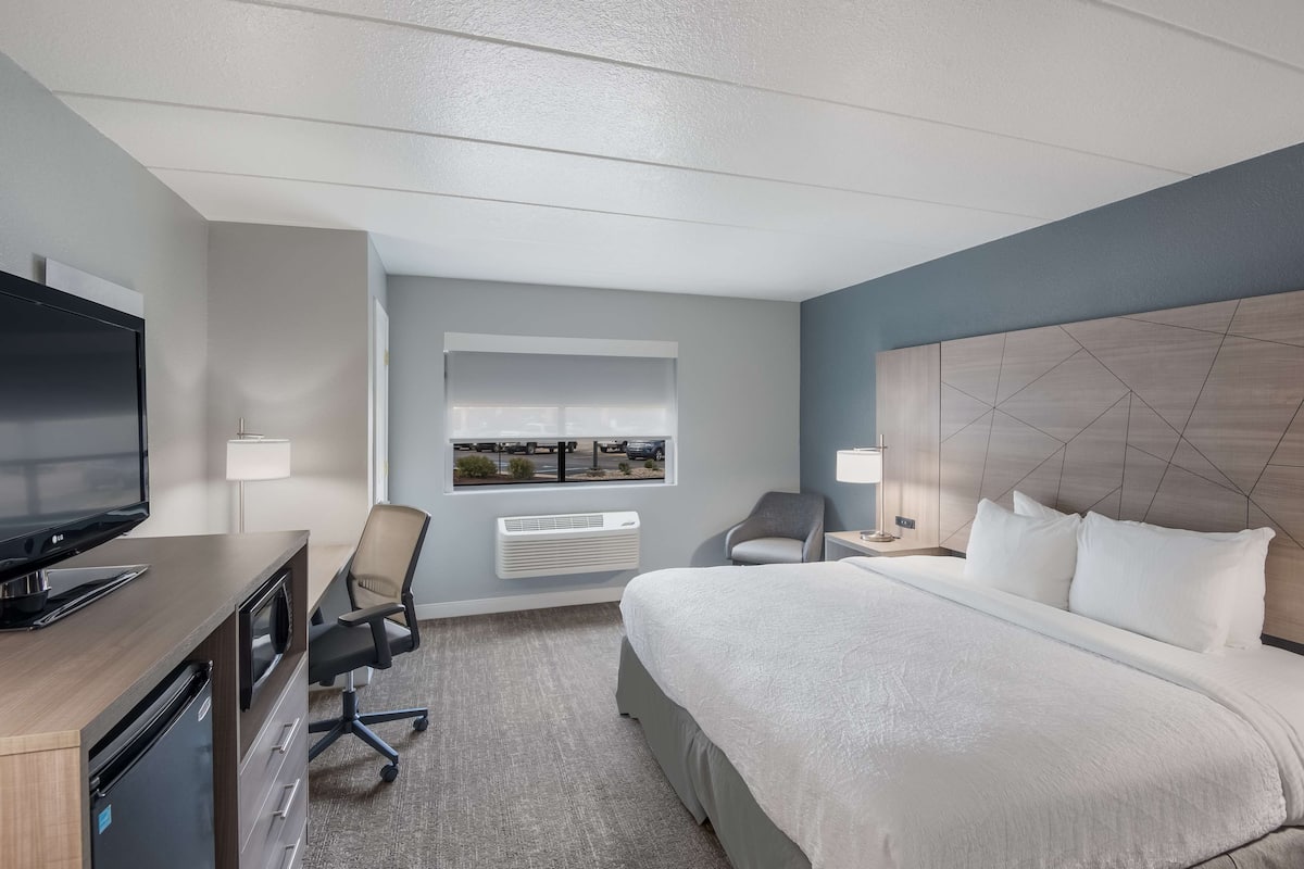 Ein Hotelzimmer mit einem Bett, einem Schreibtisch mit Fernseher, einem Sessel, einem Fenster mit Blick und einer Wand-Klimaanlage.