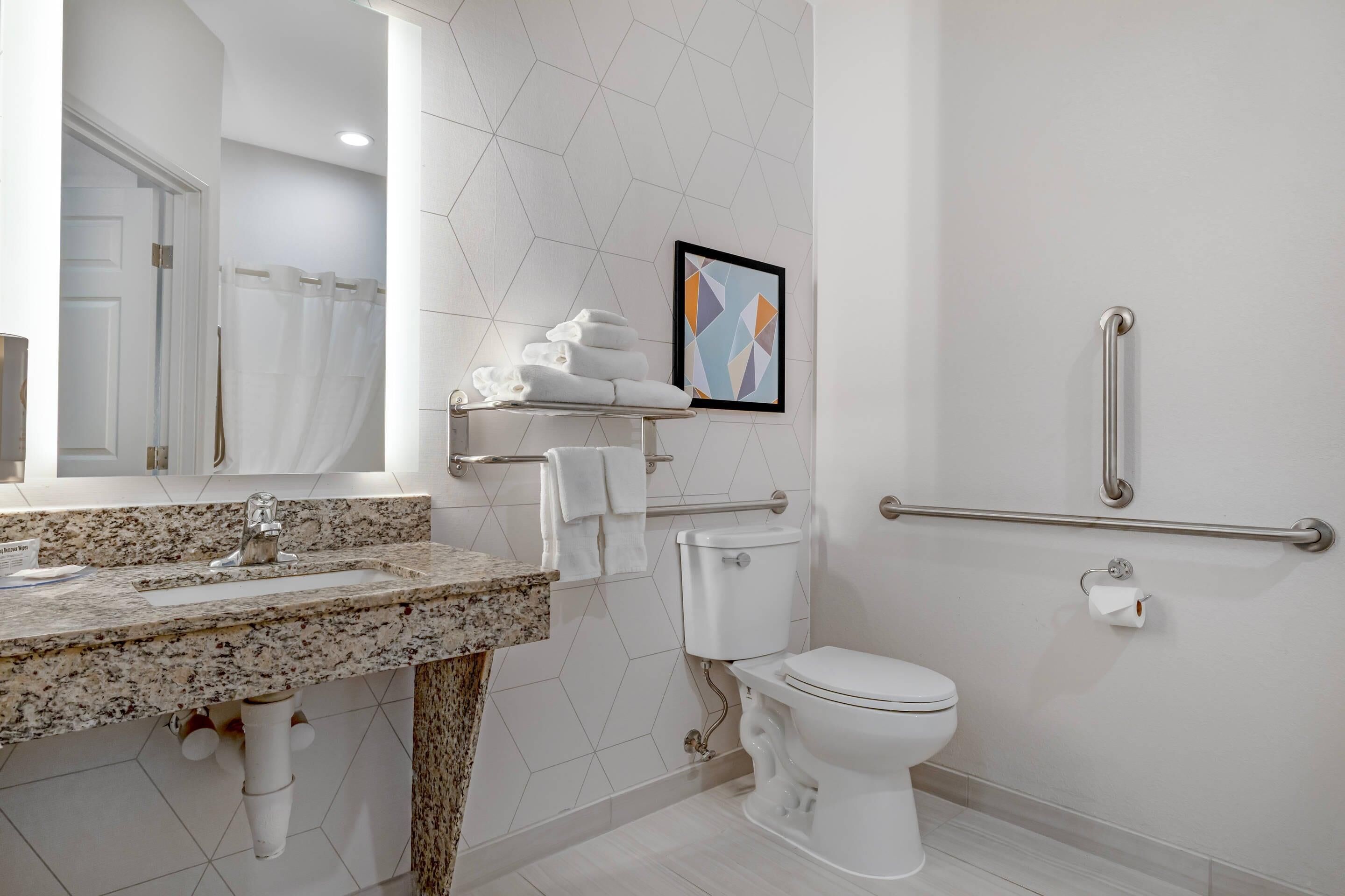Een moderne badkamer met een granieten aanrecht, toilet, een handgreep en een lijstwerk aan de muur.