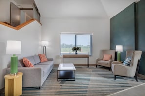 A modern living room with a sofa, two armchairs, a coffee table, and a large window offering a view of the outdoors.