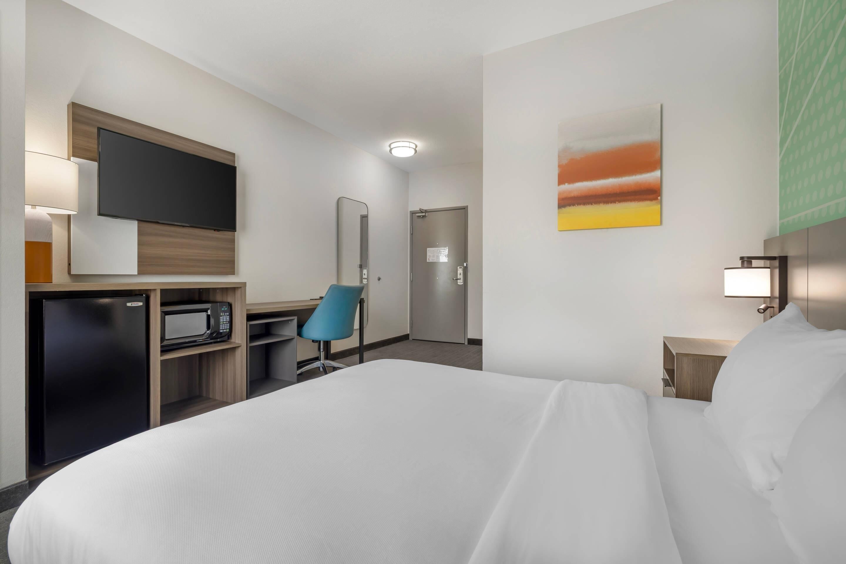 Habitación de hotel con cama, escritorio con computadora, televisión, microondas, silla y puerta.