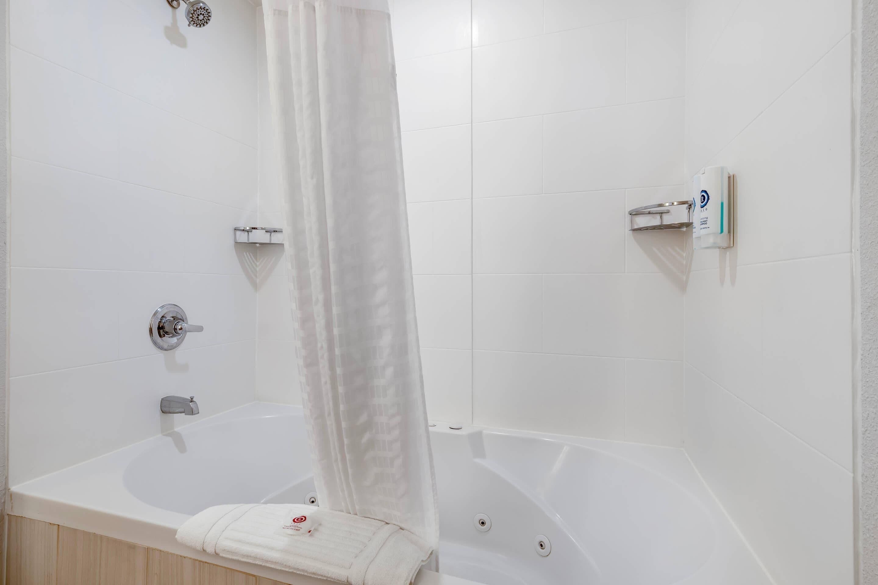 A bathroom with a bathtub, a showerhead, a towel, and a soap dispenser.