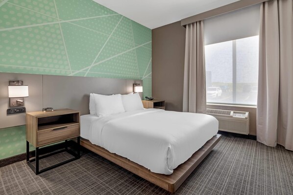 Une chambre d’hôtel comprenant un lit, des tables de chevet, des lampes, une fenêtre avec des rideaux et un mur orné d’un motif géométrique.