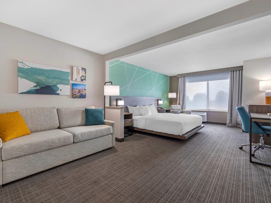 Habitación de hotel con cama, escritorio, sillón, sofá y obras de arte en las paredes.