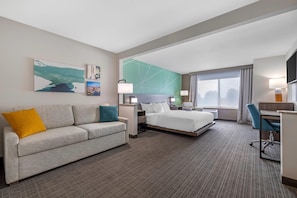 A hotel room with a bed, a desk, a chair, a sofa, and artwork on the walls.
