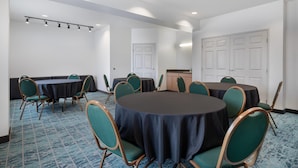A conference room with round tables and chairs, white walls, and a carpeted floor.