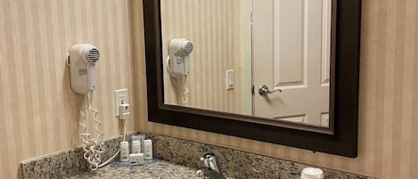 A bathroom with a granite sink, a mirror, and two hair dryers mounted on the wall.