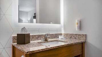 Uma casa de banho com uma pia de mármore, um espelho, um dispensador de toalhas e uma caixa de lenços.