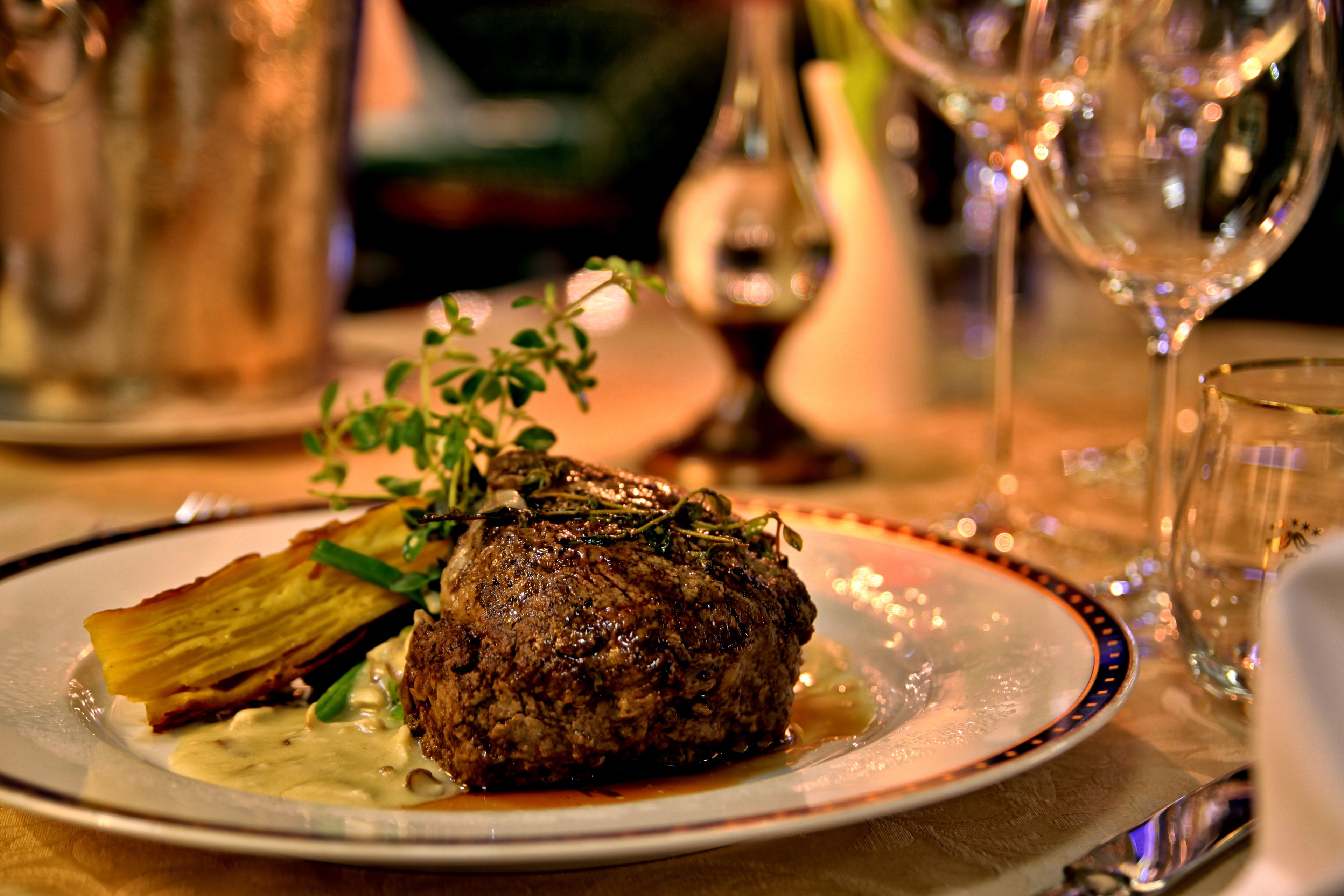 A plate with a steak, a slice of potato, and a garnish, accompanied by a glass of wine.