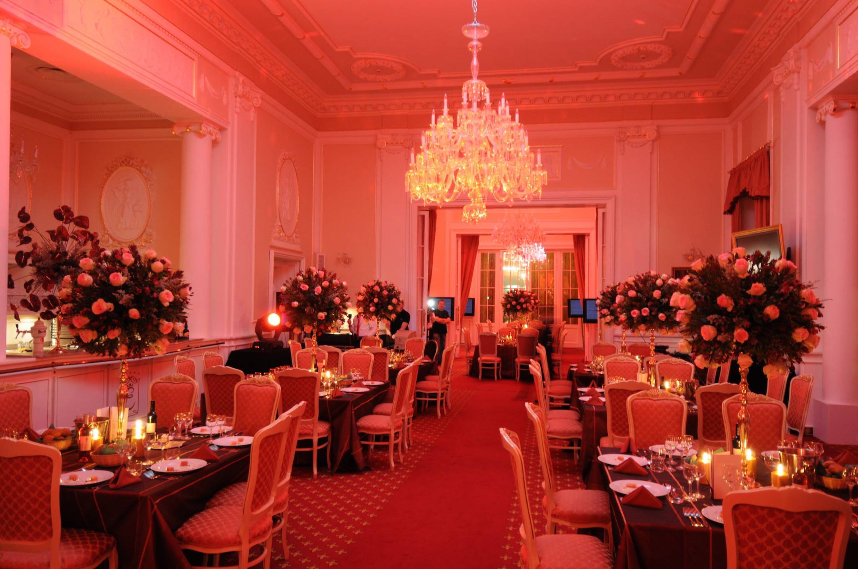 Un comedor elegante con candelabros, centros de mesa florales y alfombra roja.