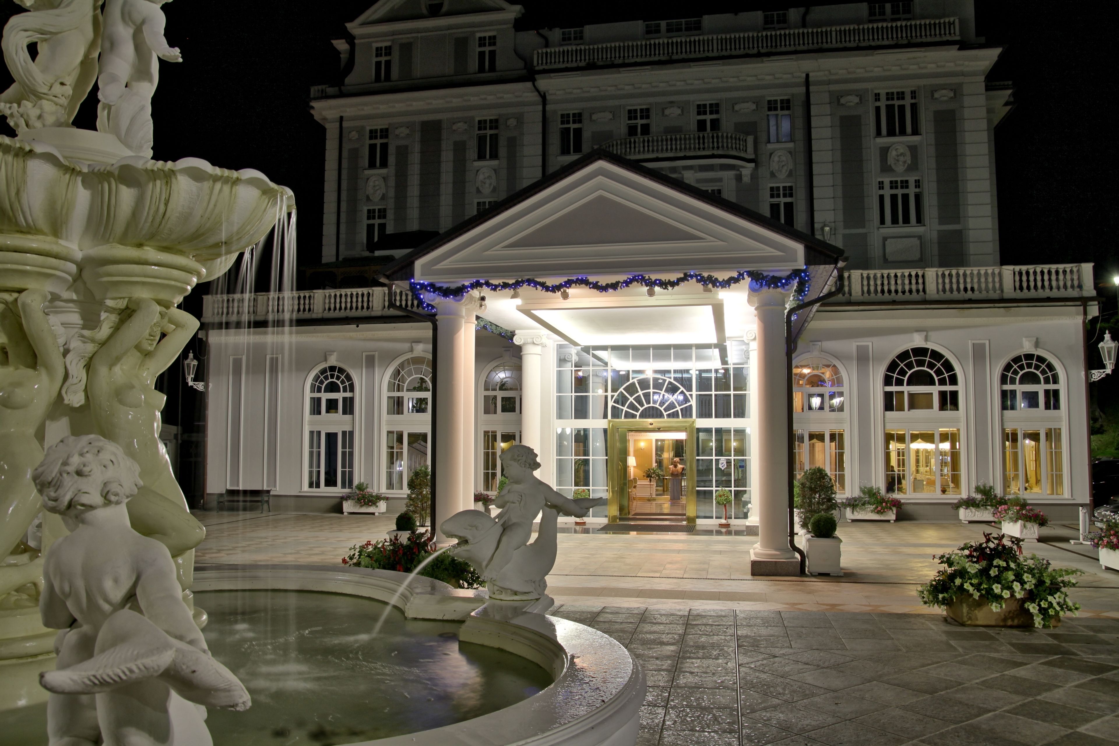 A grand hotel entrance with a fountain, large columns, and a well-maintained garden.