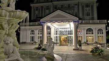 A grand hotel entrance with a fountain, large columns, and a well-maintained garden.