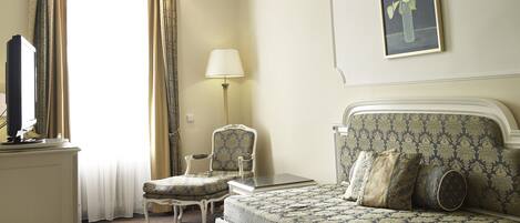 A hotel room with a bed, a chair, a desk, a lamp, and a painting on the wall.