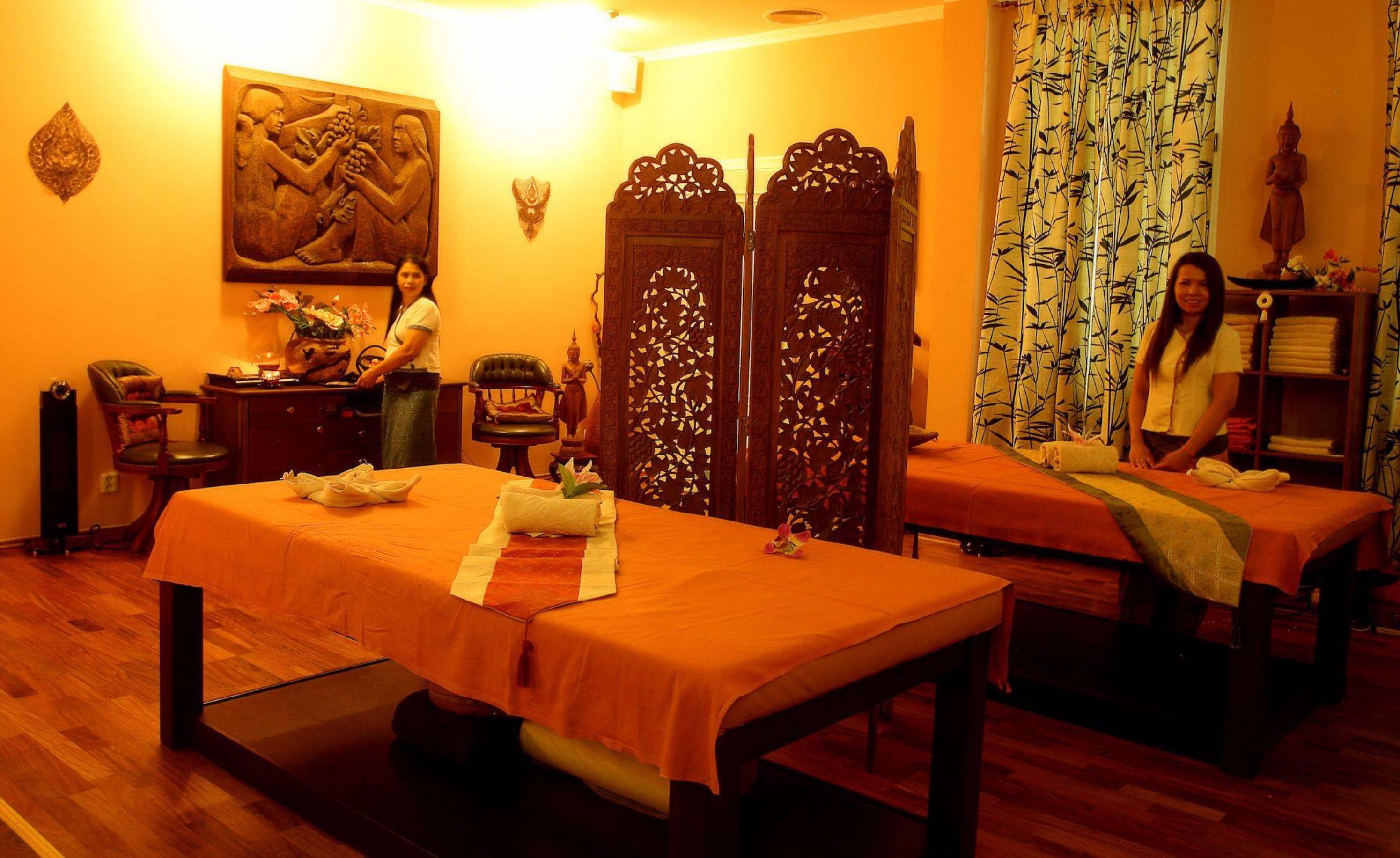 A room with two massage tables, a wooden cabinet, a statue, and a decorative screen.