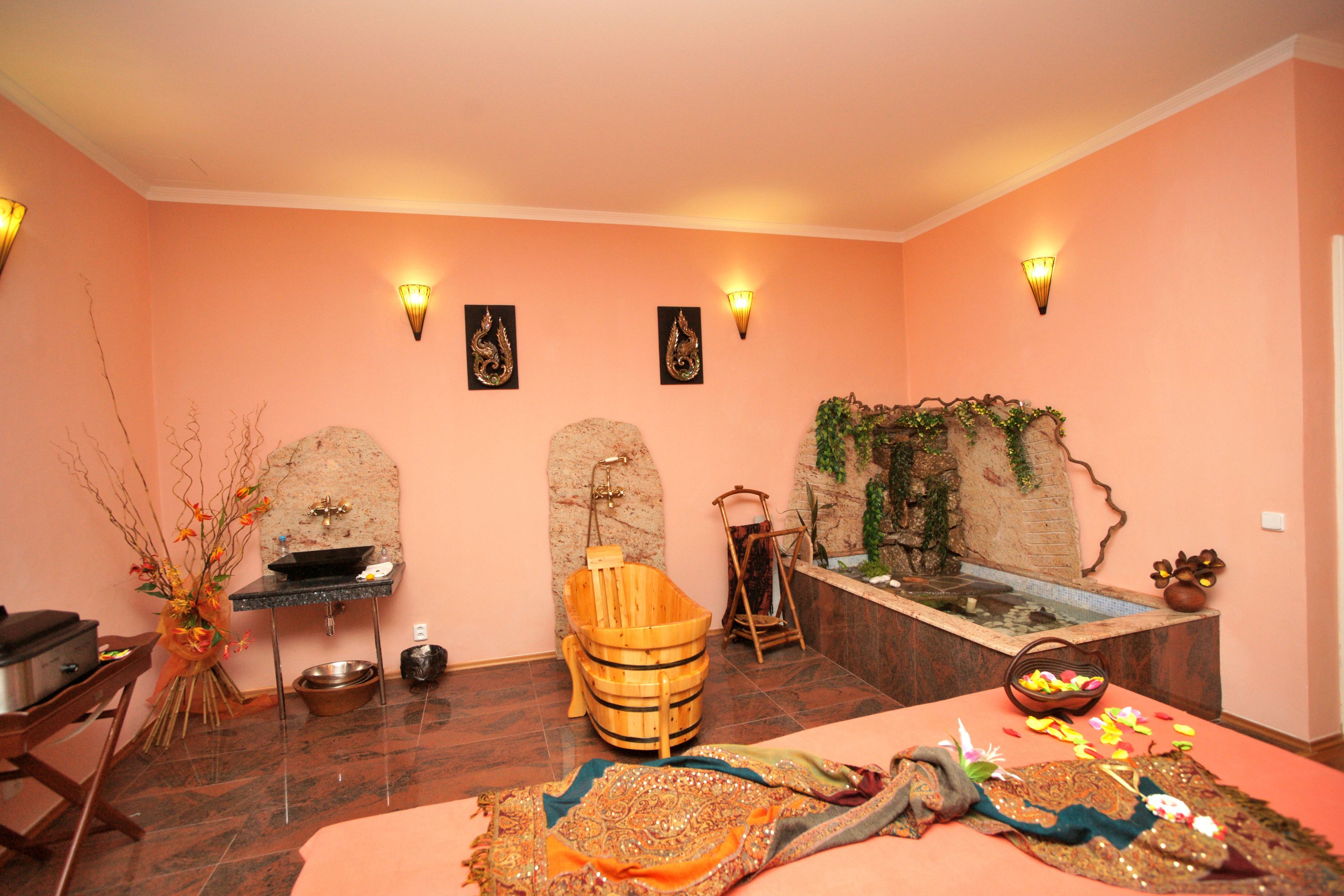 Un cuarto de spa con bañera, un bano de pies de madera, una pequeña fuente y un tapete decorativo.