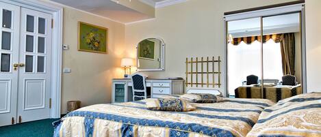 A hotel room with a large bed, a desk with a lamp, a mirror, and a wardrobe.
