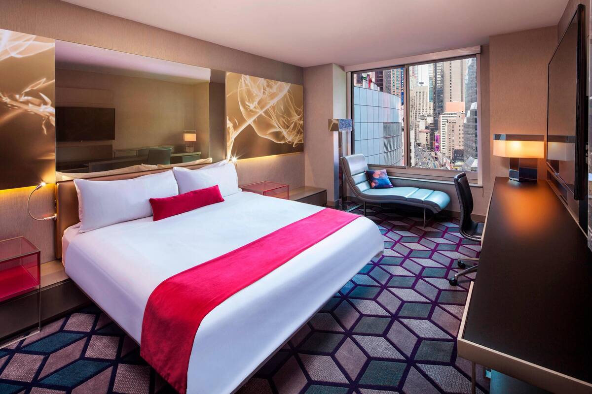 Una habitación de hotel con una cama grande, un escritorio, una silla y vistas a la ciudad.