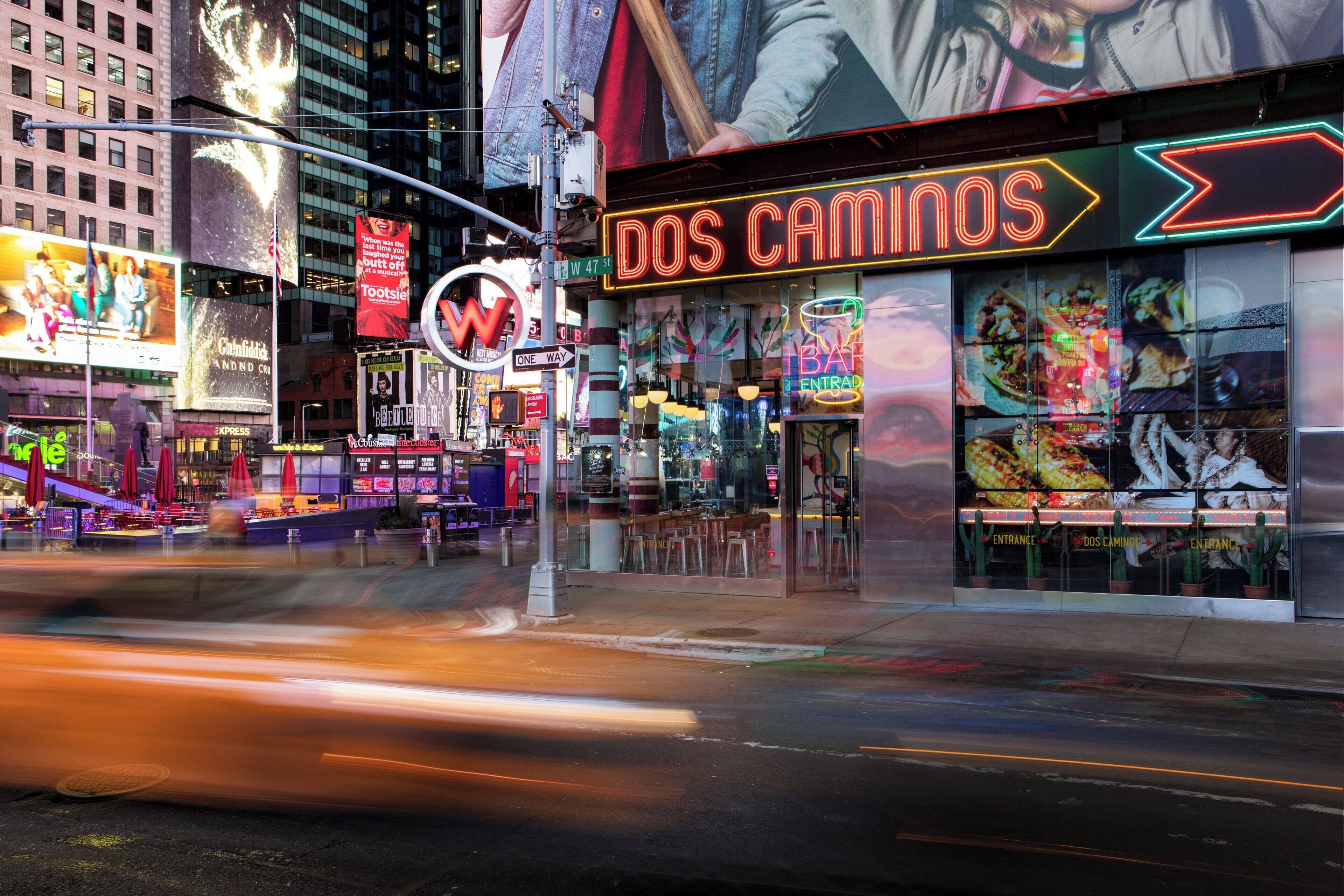 Une rue animée, illuminée de mille feux, avec une enseigne au néon pour le restaurant « Dos Caminos ».
