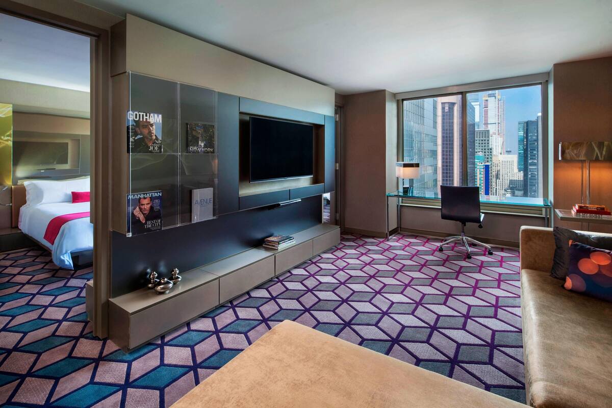 Habitación de hotel con televisor grande, cama, sofá, escritorio y vista a la ciudad.