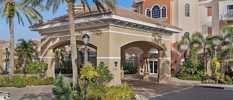 A hotel entrance with a covered patio, palm trees, and a well-maintained garden.