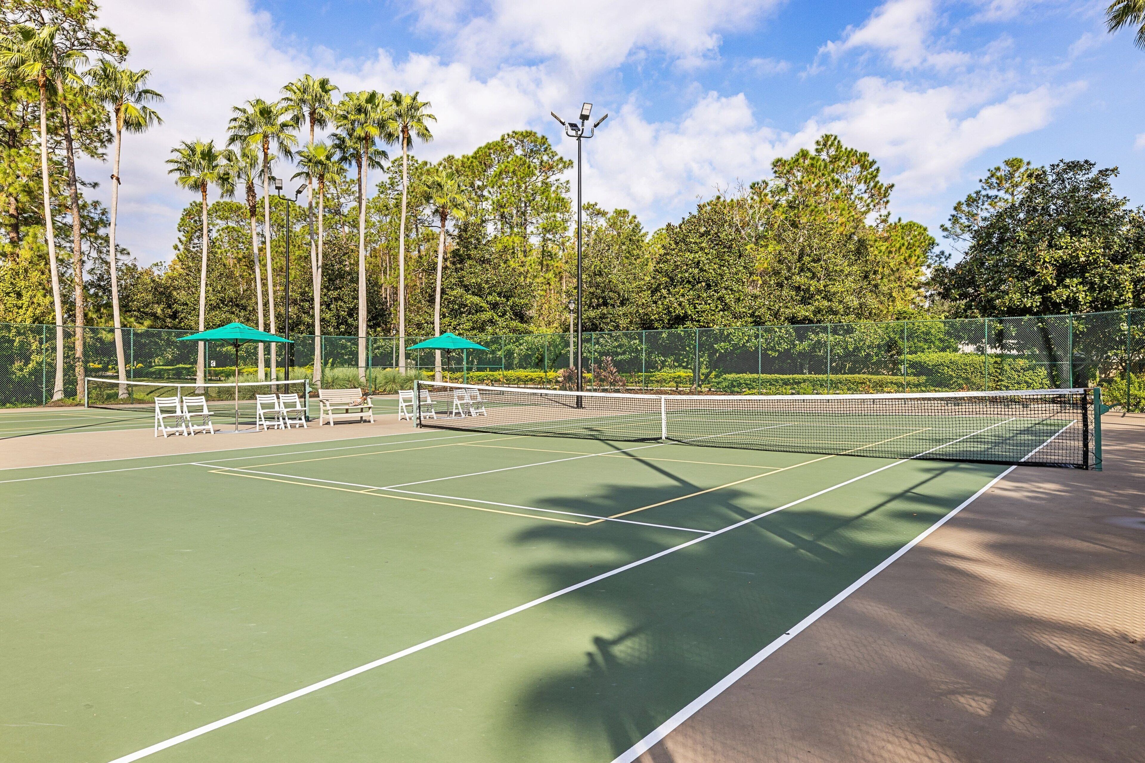 An outdoor tennis court with a net, benches, and umbrellas.